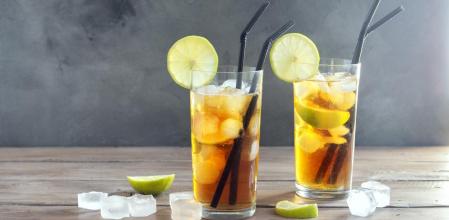 Iced Tea with lime and ice cubes over wooden background, copy space. Iced cold summer drink - Long Island Iced Tea Cocktail.