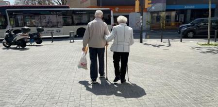 Una pareja de ancianos cogidos cariñosamente del brazo mientras andan por la calle.