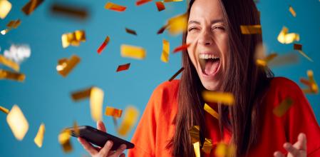 Celebrating Young Woman With Mobile Phone Winning Prize And Showered With Gold Confetti In Studio