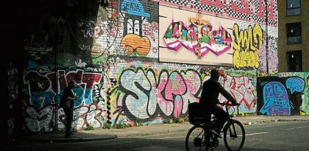 A man cycles past graffiti on in the Tower Hamlets neighborhood in London, Friday, July 22, 2022. (AP Photo/Alessandra Tarantino)