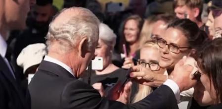 El rey Carlos III atendiendo a los fans, mientras una de ellas le regala un bolígrafo