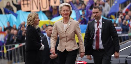 La presidenta de la Comisión Europea, Ursula von der Leyen; detrás suyo, una manifestación en favor de más armas para Ucrania
