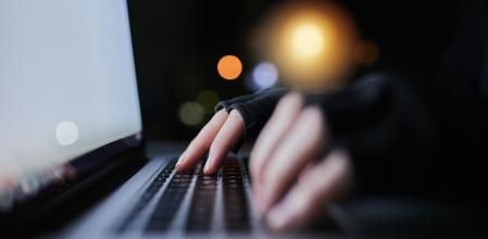 Shot of an unrecognizable computer hacker using a laptop late at night