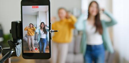 Asian young woman with her friend tiktoker created her dancing video by smartphone camera together. To share video to social media application