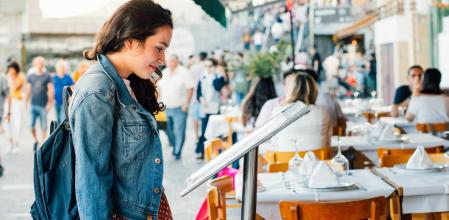 Young tourist woman looking the menu of a restaurant with terrace in the seaport of San Sebastian, Spain, in summer.
