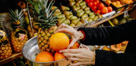 Una persona pesa cuatro piezas de naranjas y una piña en la frutería 'Vitaminas', a 2 de enero de 2023, en Madrid