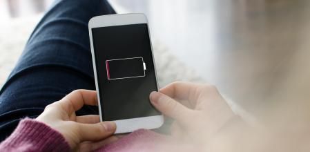 A woman is holding a mobile phone in her hands. On the device screen of the smart phone visible is an empty battery. The photo was taken over the model's shoulder. I have created the battery icon in adobe illustrator myself. It is intended to look like a generic battery icon.