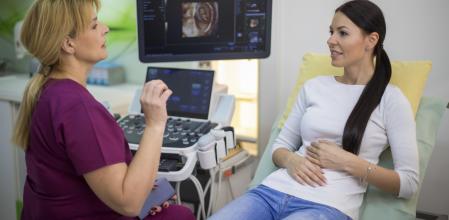 Beautiful smiling young woman patient with a senior gynecologist during the consultation in the gynecological office.Mature female doctor showing what awaits her in pregnancy.