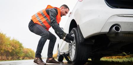 Un conductor, equipado con el chaleco reflectante, cambia una rueda del coche&nbsp;