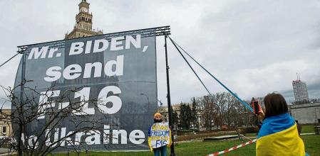 Two protestors wrapped in Ukrainian flags take images next to a sign asking U.S. President Joe Biden to send fighter jets to the Ukraine, during the president's visit in Warsaw, Poland, Wednesday, Feb. 22, 2023. Before departing Warsaw on Wednesday, Biden will hold talks with leaders from the Bucharest Nine, a collection of nations on the most eastern parts of the NATO alliance that came together in response to Russian President Vladimir Putin's 2014 annexation of Crimea from Ukraine. (AP Photo/Michal Dyjuk)