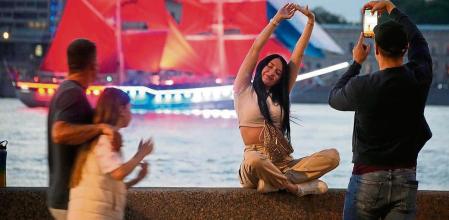 A woman poses for a photo as a brig with scarlet sails floats behind her on the Neva River during a rehearsal for the Scarlet Sails festivities marking school graduation in St. Petersburg, Russia, Friday, June 23, 2023. (AP Photo/Dmitri Lovetsky)