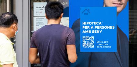Un joven mira publicidad de una hipoteca en el escaparate de una entidad bancaria