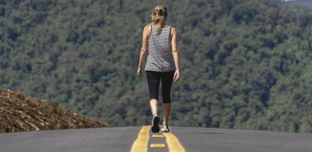 Back of a woman walking alone along a road surrounded by green mountains