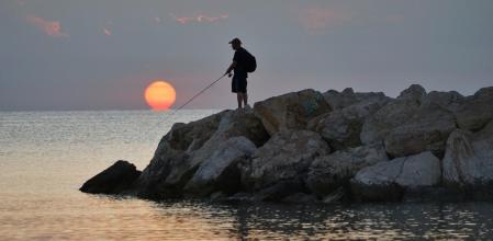Un pescador pescando el sol deformado por el efecto Omega, en Fuengirola.