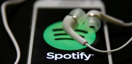 Unos auriculares encima de la pantalla de un móvil con el logo de Spotify, en una imagen de archivo