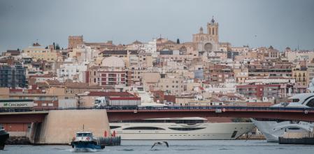 Una barca saliendo del puerto, con el puente móvil, los grandes yates de la Marina Port Tarraco y la ciudad de fondo