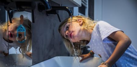 Un menor bebiendo agua de un grifo