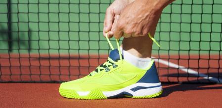 Una persona atándose los cordones de las zapatillas en una cancha de pádel.