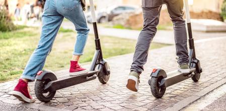 Dos personas yendo por la calle con un patinete eléctrico.