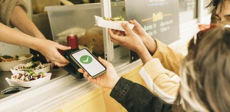 Woman paying via tap to pay method through smart phone while buying food from concession stand