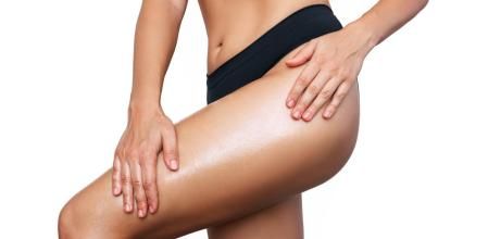 Una mujer aplicándose aceite anticelulítico en las piernas.