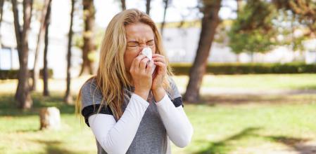 Springtime allergies. Middle aged mature woman sneezing in a park, allergic, copy space