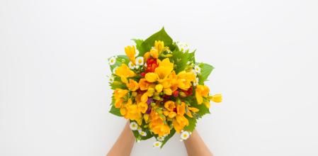 Young adult woman hands holding beautiful fresh yellow freesia flower bouquet on white table background. Point of view shot. Closeup. Top down view.