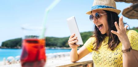 Mujer tomando algo en la playa y se sorprende gratamente cuando ve las ofertas de la semana