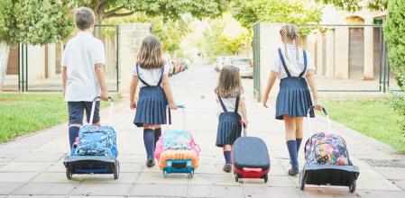 Cuatro niños con sus mochilas con ruedas que van al colegio
