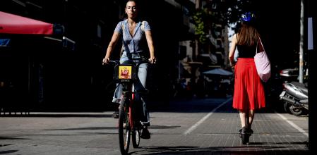 Una joven se desplaza en bicicleta y otra en patinete eléctrico por el carril bici de de Gran Vía, entre plaza Cerdà y plaza Espanya, en Barcelona&nbsp;
