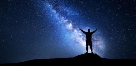Milky Way with silhouette of a standing happy man with raised up arms on the mountain. Night landscape with beautiful galaxy. Universe. Night sky with stars and colorful  Milky Way. Bright stars