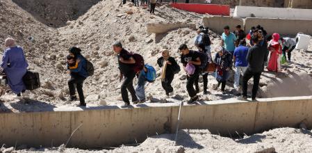 People carry their belongings while walking on the rubble, after an Israeli strike, as they flee Lebanon due to ongoing hostilities between Hezbollah and Israeli forces, at Masnaa border crossing with Syria, in Lebanon, October 4, 2024. REUTERS/Mohamed Azakir