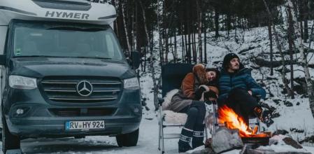 Una pareja junto a una pequeña hoguera para calentarse en una acampada invernal