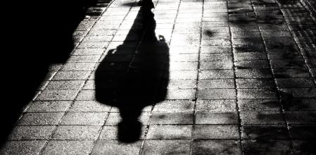 Blurry shadow and silhouette of a man standing in the night on wet city street sidewalk with water reflection in black and white