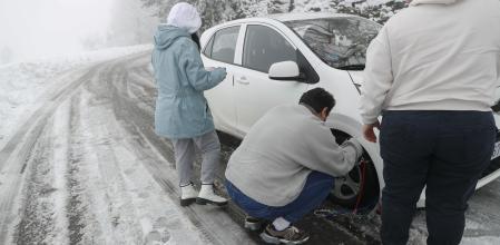 Varias personas colocan las cadenas para circular por una carretera cubierta de nieve, este jueves 20 de noviembre de 2025, en Pedrafita do Cebreiro.