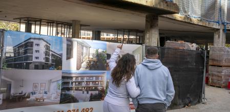 UNA PAREJA DE JOVENES OBSERVA UNA PROMOCIÓN DE VIVENDAS EN EL CENTRO DE RUBÍ.