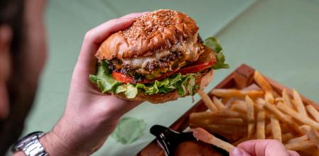 Un hombre sostiene una hamburguesa con queso y beicon frito