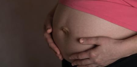 Young pregnant between 30 and 35 years old woman touches her belly. Dramatic light. Closeup