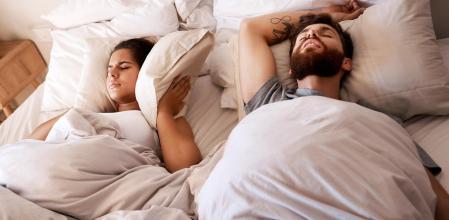 Una pareja en la cama y ella se tapa los oídos porque él está roncando