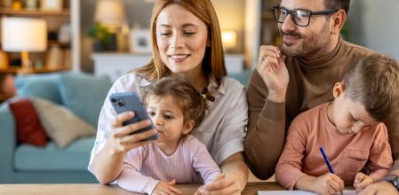 Una familia mirando el móvil mientras el niño escribe en una libreta
