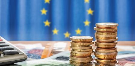 Monedas y billetes frente al logo de la Unión Europea