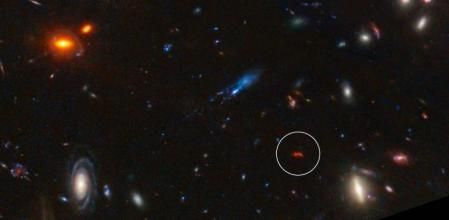 La galaxia MACS0416 Y1 brilla, en esta toma del telescopio espacial James Webb, gracias a la luz emitida por el polvo calentado por nuevas estrellas