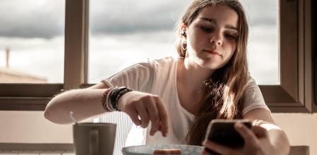 Adolescente desayunando mientras mira el móvil.
