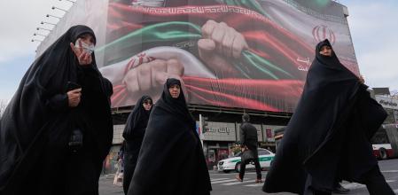 Un grupo de mujeres cruza la calle bajo una pancarta que muestra manos que sostienen banderas iraníes en señal de patriotismo, mientras una de ellas hace el signo de la victoria, en Teherán&nbsp;
