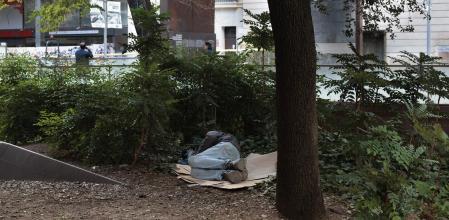 Una persona sin hogar descansa en la plaza de la Vila de Madrid, en Barcelona 