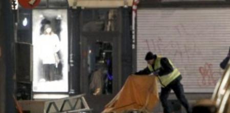 Un policía tapa con una manta el cadáver del fallecido tras estallar dos coches por causas todavía no aclaradas en la calle Drottning de Estocolmo, una zona comercial muy importante