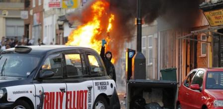 Un joven encapuchado desafía a la policia detrás de un taxi destrozado, durante los enfrentamientos vividos en el conflictivo barrio de Hackney, al este de Londres. Hackney fue hoy escenario de nuevos enfrentamientos entre la policía y un grupo de jóvenes que saquearon tiendas y atacaron autobuses. Según informó la cadena BBC, los disturbios se desencadenaron después de que la policía efectuara algunos registros en la calle, lo que dio lugar a que momentos después un grupo de encapuchados se enfrentara a los agentes arrojándoles piedras y botellas
