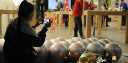 Una mujer toma fotografías con un iPhone a un improvisado arreglo de velas y flores al frente de una tienda de Apple en Santa Monica