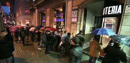 Compradores hacen cola incluso lloviendo ante la administración de lotería El Gato Negro, en la calle Pelai de Barcelona