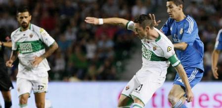 El jugador del Elche Albacar (c) dispara ante el argentino Di María (d), del Real Madrid, durante el partido de Primera División que están disputando esta noche en el estadio Martínez Valero, en Elche